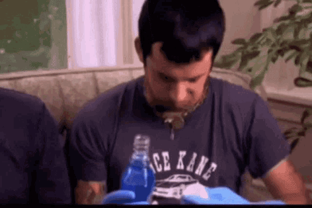 a man wearing a shirt that says ice kane is drinking from a bottle