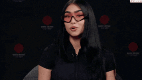 a woman wearing glasses and a black shirt is talking