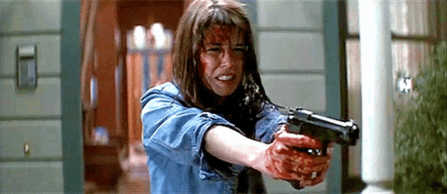 a woman is holding a gun with blood on her face .