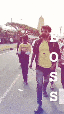 a man in a yellow shirt is walking down a street with other people .
