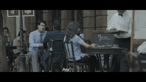 a man sitting at a table talking to a woman in front of a menu board that says menu