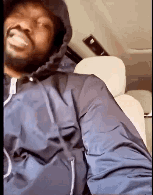 a man in a hooded jacket is sitting in the back seat of a car smoking a cigarette .