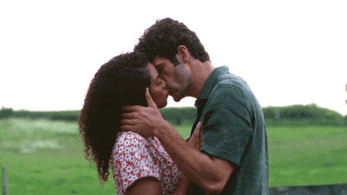 a man and woman kissing in front of a green field