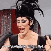 a drag queen is wearing a black feathered hat and a black dress .