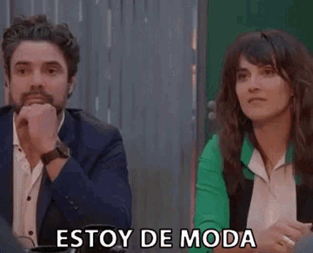 a man in a suit and a woman in a green jacket are sitting at a table with the words estoy de moda above them