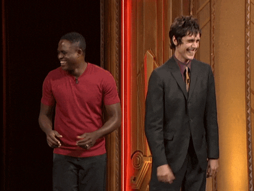 a man in a suit and a man in a red shirt are laughing together