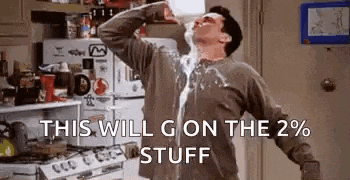 a man is drinking milk from a bottle while standing in a kitchen with his arms outstretched .