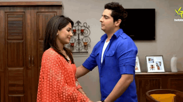 a man in a blue shirt and a woman in an orange dress are standing next to each other in front of a hotstar logo