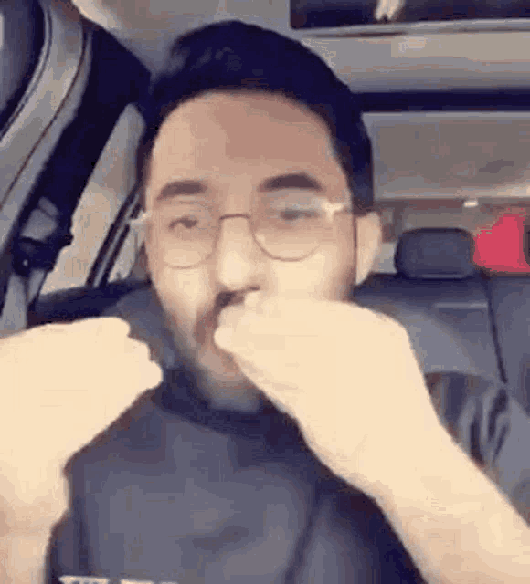 a man wearing glasses is sitting in the back seat of a car and smelling his nose .