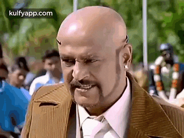 a bald man with a beard and mustache is wearing a suit and tie and making a funny face .