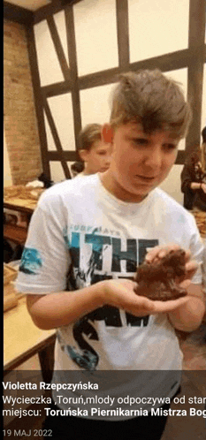 a young boy in a white shirt is holding a small animal in his hands .