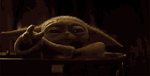 a close up of a baby yoda in a dark room looking at the camera
