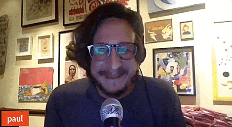 a man wearing glasses and headphones is talking into a microphone in front of a wall of paintings and a paul logo