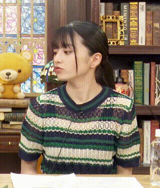 a woman in a striped shirt is sitting at a table in front of a bookshelf with a teddy bear .