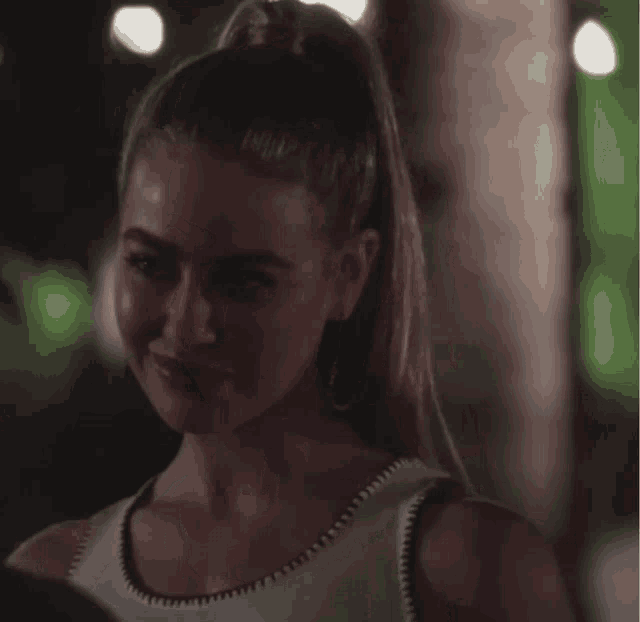 a woman with a ponytail is smiling and wearing a white top