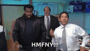 a man in a suit and tie is running in a room with other men and says hmfny .