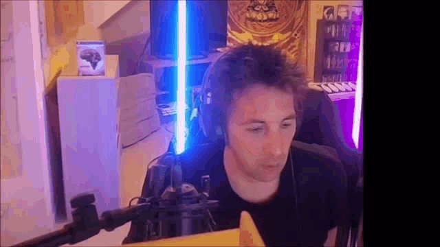 a man wearing headphones is sitting in front of a microphone with a light saber in his hand .