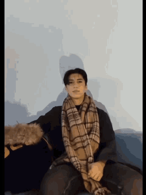 a young man wearing a plaid scarf is sitting on a couch
