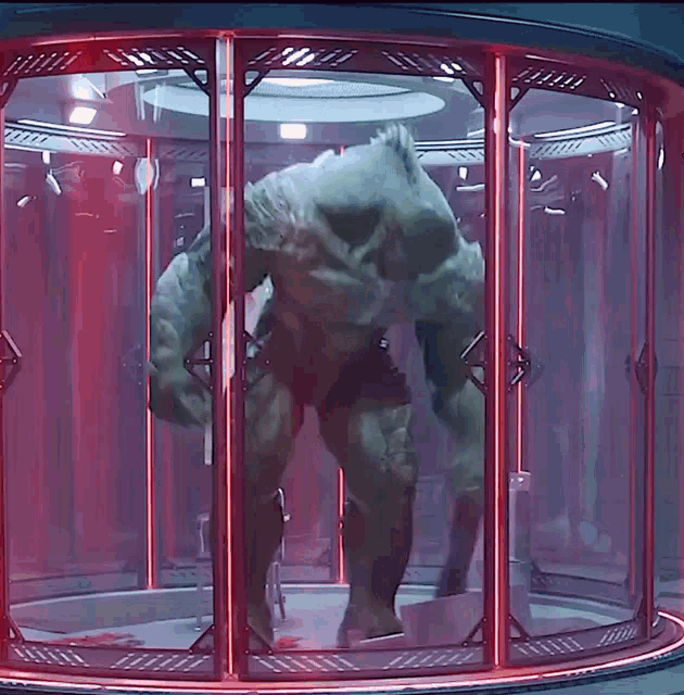 a green monster is standing in a glass cage with red lights