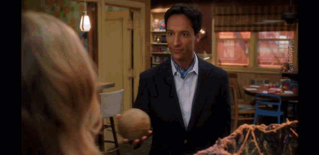 a man in a suit holds an apple in front of a woman in a kitchen