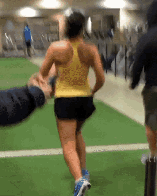 a woman in a yellow tank top and black shorts is running on a grassy field