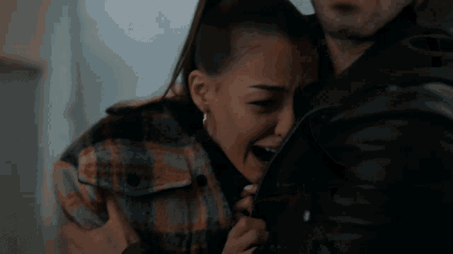 a woman is crying while being held by a man in a black jacket