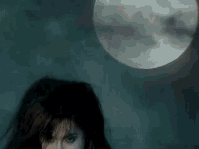a woman in a dark room with a full moon behind her