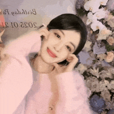 a woman in a pink sweater stands in front of a wall of flowers with the date 2022 on it