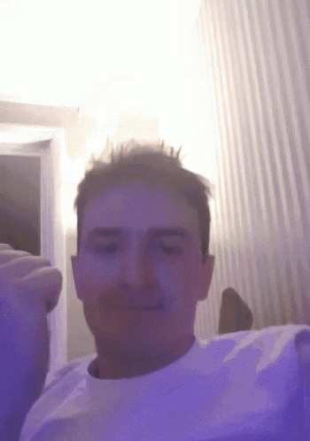 a man in a white shirt is making a funny face in a room with purple lights .