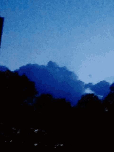 a dark blue sky with a few clouds and trees in the foreground