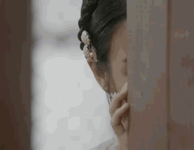 a woman covering her face with her hand behind a wooden wall