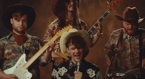 a man in a cowboy hat is singing into a microphone while two other men play guitars