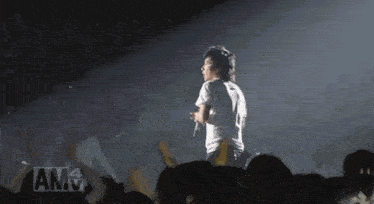 a man in a white shirt is singing into a microphone in front of a crowd with am4 written on the bottom right
