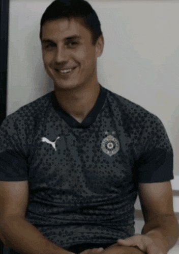 a man wearing a shirt with a puma logo on it is smiling