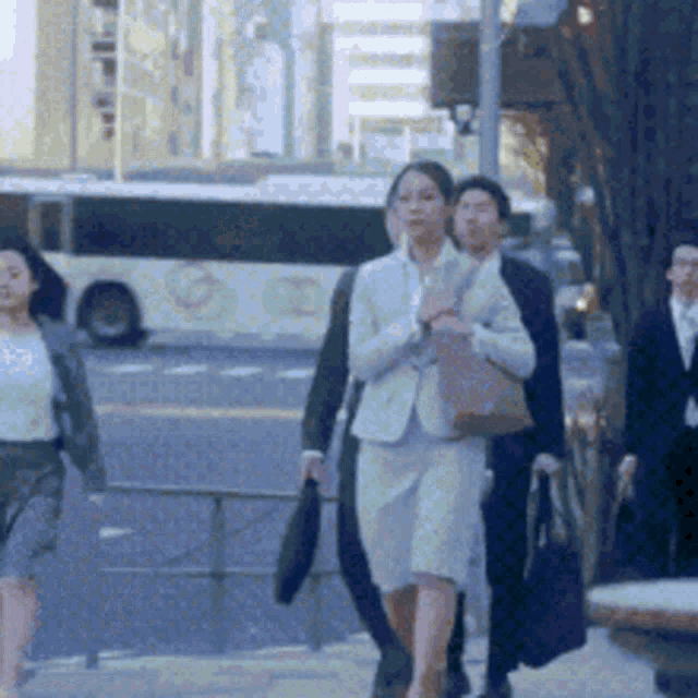 a group of people are walking down a sidewalk with a bus in the background