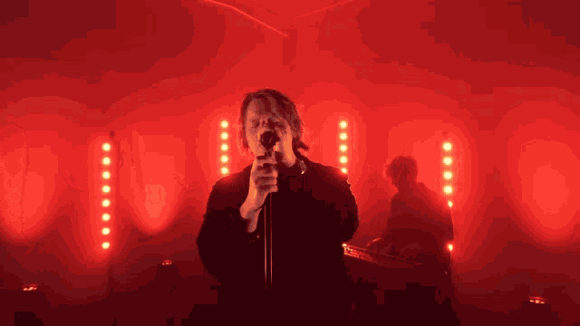 a man singing into a microphone in a dark room with red lights
