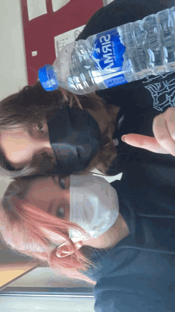two people wearing face masks and holding a bottle of water that says nissin on it