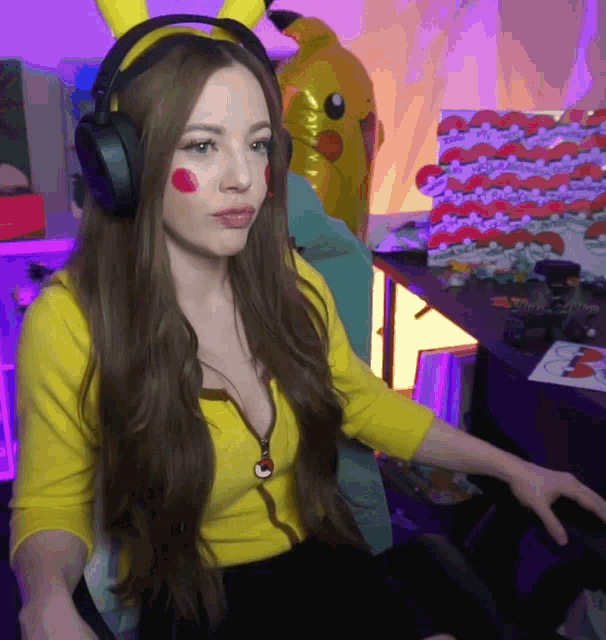 a woman wearing headphones and a yellow shirt is sitting in front of a pikachu balloon