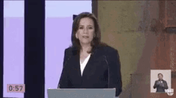 a woman is giving a speech at a podium with a countdown of 0:57 behind her .