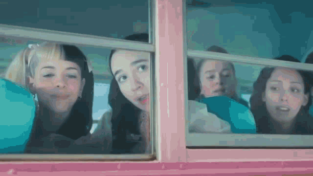 a group of young women are looking out of a pink school bus window .