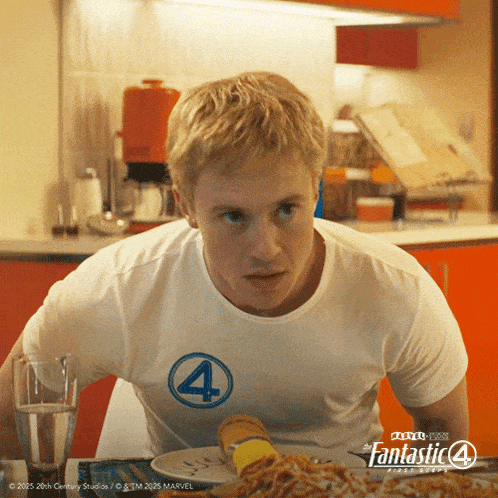 a man wearing a fantastic 4 t-shirt sits at a table with a plate of food