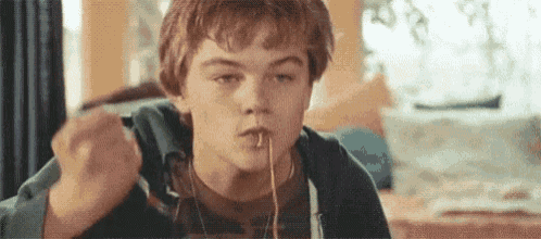 a young man is eating spaghetti with a fork while sitting at a table .