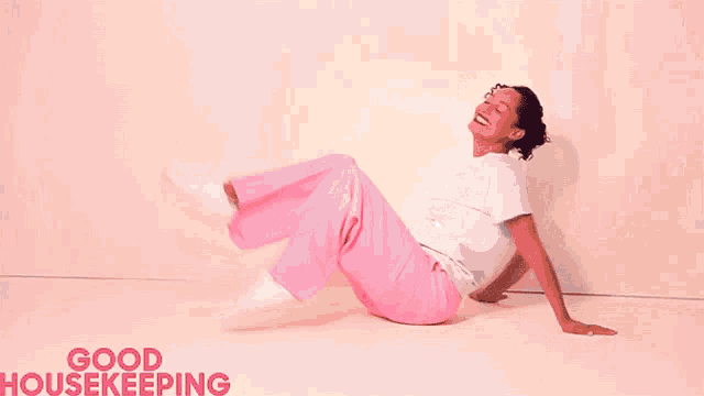 a woman in pink pants is sitting on the floor with the words good housekeeping behind her .