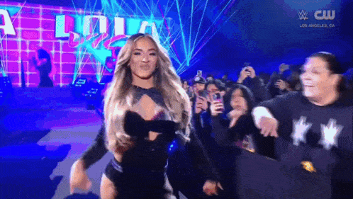 a woman is walking on a stage in front of a crowd while wearing a black top .