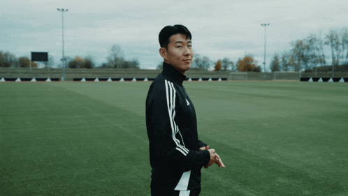 a man in an adidas jacket is standing on a soccer field