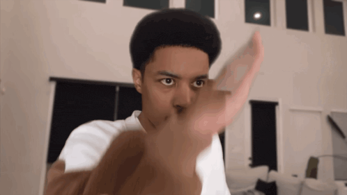 a young man in a white shirt is pointing his finger at the camera