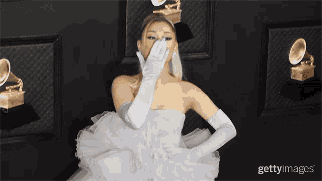 a woman in a white dress and white gloves covers her face with her hand