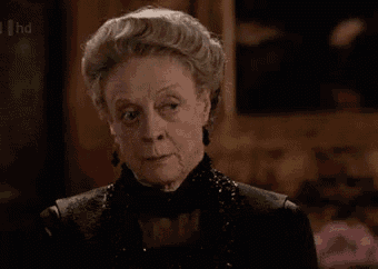 an older woman with gray hair is wearing a black dress and earrings and looking at the camera .