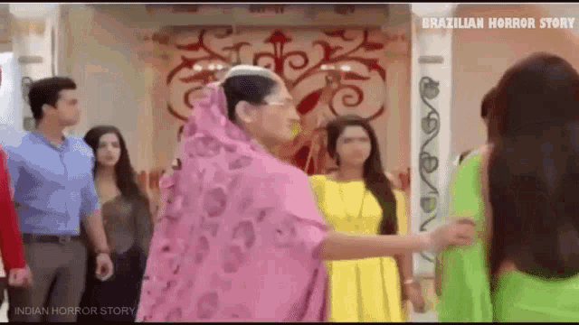 a group of people are standing in a room with a woman in a pink dress .