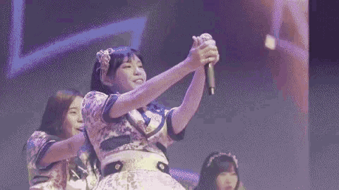 a girl is taking a selfie with a microphone while another girl stands behind her .